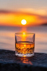 Wall Mural - A glass of whiskey catches the golden glow of a sunset by the water, creating a warm and serene atmosphere.