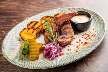 Wall Mural - A vibrant plate featuring grilled tongue and potatoes, accompanied by pickles, red onions, and a dipping sauce. Perfect for food-related projects showcasing delicious meals.