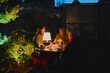 © amixstudio - Happy elderly couple and their adult daughter celebrate holiday in the courtyard of the house, family of three have dinner in lamplight