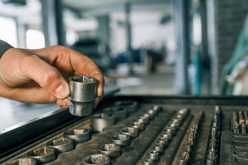Poster - Hand selecting a metal socket wrench piece from an organized tool tray in a workshop setting, symbolizing precision and automotive repair