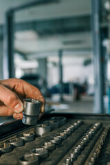 Poster - Hand selecting a metal socket wrench piece from an organized tool tray in a workshop setting, symbolizing precision and automotive repair