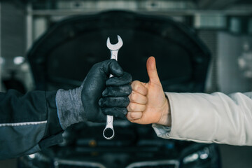 Poster - Close-up of a mechanic's gloved hand holding a wrench and a customer's hand giving a thumbs-up, symbolizing satisfaction and trust in car repair services