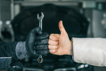 Poster - Close-up of a mechanic's gloved hand holding a wrench and a customer's hand giving a thumbs-up, symbolizing satisfaction and trust in car repair services