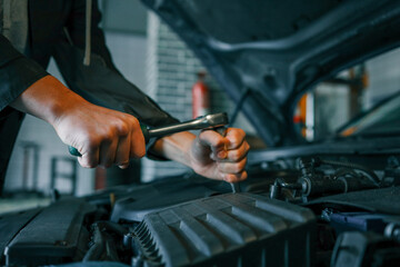 Fototapete - Close-up of a mechanic's hands using a wrench to perform maintenance on a car engine in a workshop setting