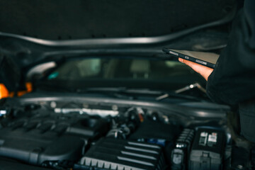 Aufkleber - A mechanic holding a tablet while inspecting a car engine in a workshop. The focus is on the integration of modern technology in vehicle diagnostics and repair