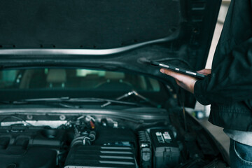 Aufkleber - A mechanic holding a tablet while inspecting a car engine in a workshop. The focus is on the integration of modern technology in vehicle diagnostics and repair