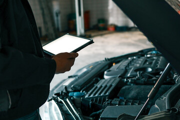 Aufkleber - A mechanic holding a tablet while inspecting a car engine in a workshop. The focus is on the integration of modern technology in vehicle diagnostics and repair