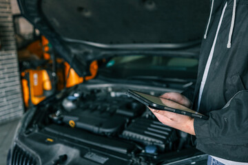 Aufkleber - A mechanic holding a tablet while inspecting a car engine in a workshop. The focus is on the integration of modern technology in vehicle diagnostics and repair