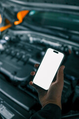 Aufkleber - Mechanic holding a smartphone with a blank white screen in front of an open car engine for diagnostics or maintenance. Indoor workshop setting