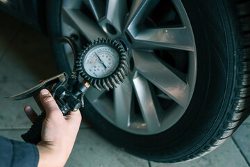 Aufkleber - A mechanic checks tire pressure with a gauge during routine car maintenance in a garage. Focus on the wheel and the instrument ensuring optimal vehicle safety and performance