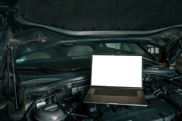 Fototapete - Laptop placed on a car engine under an open hood in a garage. Represents modern automotive diagnostics and maintenance using computer technology