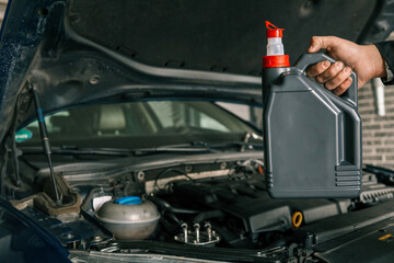 Fototapete - Close-up of a mechanic holding a bottle of motor oil and an oil dipstick, performing an oil change in a vehicle. Highlights car maintenance and servicing tasks