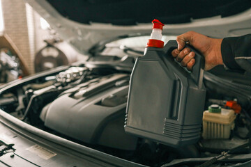 Fototapete - Close-up of a mechanic holding a bottle of motor oil and an oil dipstick, performing an oil change in a vehicle. Highlights car maintenance and servicing tasks