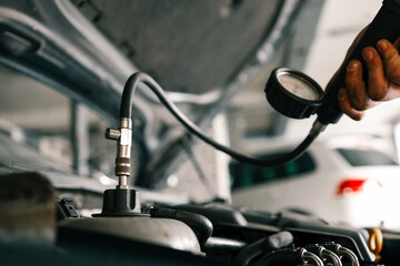 Fototapete - Mechanic using a pressure gauge to test and diagnose the engine system of a car in a workshop. Open hood reveals components and testing equipment