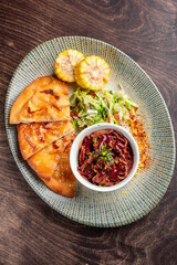 Wall Mural - A vibrant plate featuring crispy flatbreads, tender pulled meat in sauce, fresh salad, and grilled corn, all beautifully arranged on a textured platter against a wooden background.