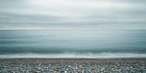 Poster - Serene beach scene featuring a tranquil overcast sky, a gradient sea, and a shoreline scattered with pebbles, creating a peaceful atmosphere for relaxation at this tranquil beach.