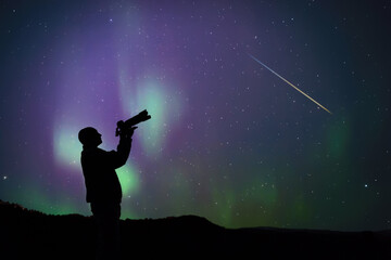 Wall Mural - man observing and photographing aurora borealis polar lights and milky way stars from a dark country
