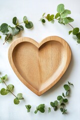 Wall Mural - A heart-shaped plate crafted from light oak wood rests on a smooth white surface. Small green leaves adorn the edges, creating a calming and organic aesthetic with ample space for text