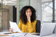 © Liubomir - Satisfied businesswoman smiling holding report in hands, office worker among papers and contracts working inside office with laptop. Financier accountant with successful achievement results.
