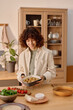 © AnnaStills - Vertical shot of young adult Caucasian woman looking at baking tray with baked potatoes covered with olive oil and herbes de Provence