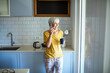 © Marko Geber - Senior woman talking on phone and drinking coffee in modern kitchen