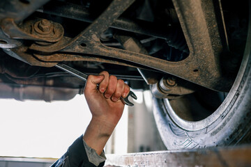 Aufkleber - Mechanic's hand holding a wrench, working underneath a car on a lift. The view shows a close-up of the suspension and exhaust system in a garage setting