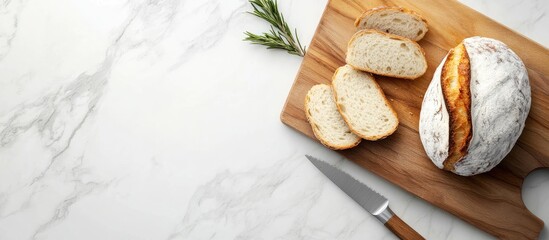 Poster - Sliced artisanal bread on a wooden cutting board with a knife and sprig of rosemary on a marble countertop Copy Space
