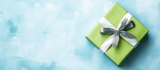 Poster - Green gift box with silver ribbon on blue textured background with copy space for holiday or celebration greetings.