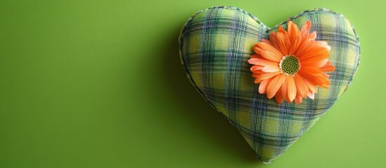 Poster - Heart-shaped pillow with plaid design decorated with an orange flower on a green background Copy Space