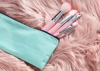 Set of makeup brushes in cosmetic bag on pink fur background