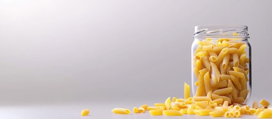 Poster - Dried pasta in a glass jar with scattered pieces on a light background and ample copy space