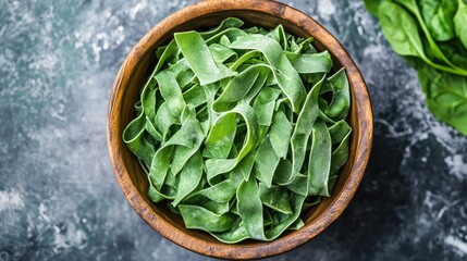 Poster - Fresh green ribbon pasta in a wooden bowl placed on a textured stone surface Copy Space