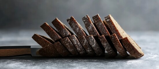 Poster - Sliced dark bread arranged at an angle with a knife on a textured gray surface Copy Space