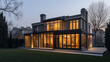 © Pierre Villecourt - Maison moderne à deux étages avec grandes fenêtres vitrées, extérieur sombre, éclairage intérieur chaleureux, patio spacieux et pelouse paysagée au crépuscule