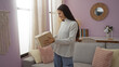 © Krakenimages.com - Woman holding package in cozy living room with pink walls, macrame wall hanging, and beige curtains, smiling and looking at the box.
