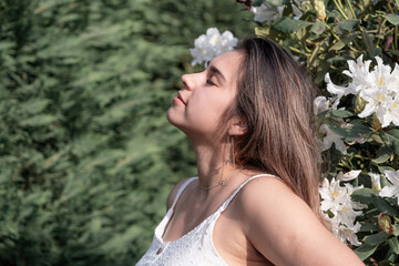 Wall Mural - beautiful young woman wearing white summer dress surrounded by white rhododendron blossom