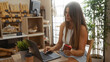 © Krakenimages.com - Young, attractive, hispanic, woman using laptop and phone in a bakery shop with bread and pastries in the background.