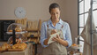 © Krakenimages.com - Young woman taking notes in a bakery shop with various pastries and loaves of bread on display.