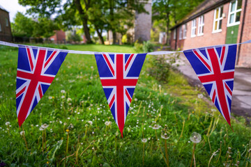 English Union Jack flags bunting, UK flag banner hanging, waving in York old church courtyard, school yard in the background on a sunny day, no people. England travel, patriotic, pride backgrounds. 