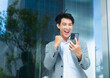 © kan - Excited Happy Asian businessman looking at mobile phone screen, celebrating successful, overjoyed, win and victory, job promotion after reading good news in online messages and email on smartphone.
