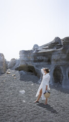 Wall Mural - Woman standing outdoors on rocky terrain in lanzarote, canary islands, wearing a white dress and holding a straw bag