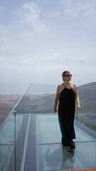 Wall Mural - Young woman sightseeing on a scenic glass walkway in haria, lanzarote, surrounded by mountains and valleys under a partially cloudy sky.