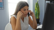 © Krakenimages.com - Young woman talking on phone in workplace looking concerned while sitting at desk in modern office with plant in background