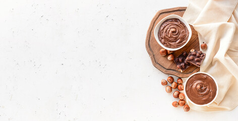 Canvas Print - Bowls with tasty chocolate paste and hazelnuts on light background