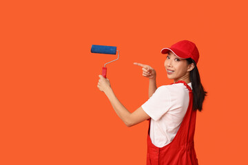 Wall Mural - female asian painter pointing at roller on orange background