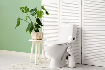 Wall Mural - Interior of restroom with toilet bowl, folding screen and houseplant near green wall