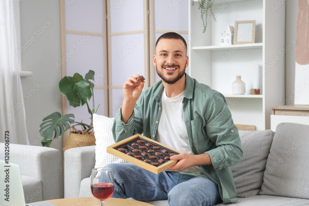 Young man with box of chocolates sitting on sofa at home