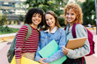 © Xavier Lorenzo - Three young university female students smiling together at camera on campus, holding folders and backpacks, enjoying their university experience. Education lifestyle and youth concept