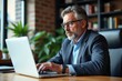 © NeedMoreMars - Focused Middle-Aged Businessman Working from Home on Laptop in Cozy Office Environment Surrounded by Plants and Bookshelves