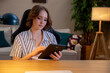 © fotodrobik - A young woman is engaged deeply with a tablet while relaxing in a modern living space